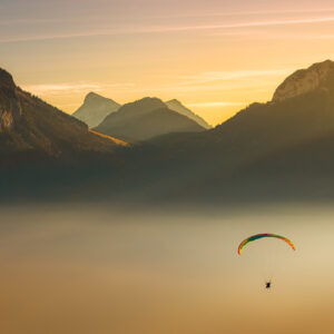 paraglider flys over lake Annecy in France covered by golden mist, with mountains in the background