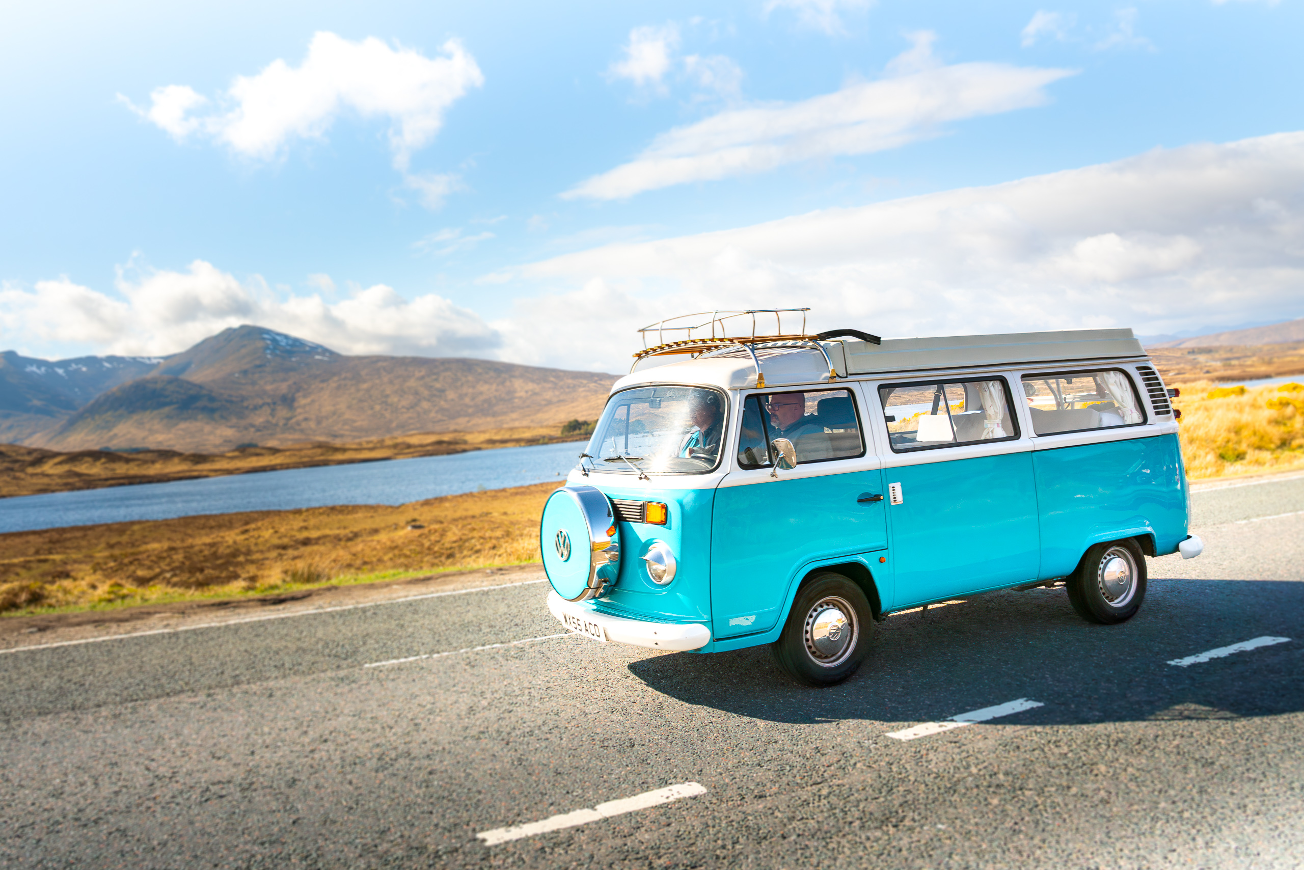 An old retro blue Volkswagen camper van driving on a countryside road in Scotland